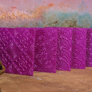 May include: A set of four rectangular purple textured sheets featuring distinct embossed patterns. The designs include repeating floral motifs, layered circular shapes, and fan-like arrangements, all rendered in a vibrant, solid purple color.