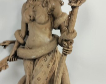 May include: A brown ceramic sculpture of a woman with a crown of thorns, holding a staff with a skull on top. The woman is wearing a long flowing robe with a snake wrapped around her waist.