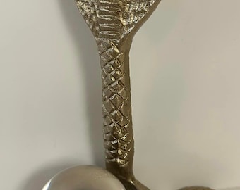 Könnte beinhalten: Eine goldfarbene Metallskulptur einer Kobra mit einer klaren Glaskugel, die in ihren Windungen ruht.
