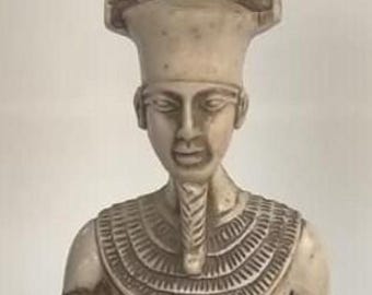 Peut inclure: Statue crème d'une figure égyptienne, avec une haute coiffe à motif quadrillé. La figure a un visage détaillé, un collier et un vêtement en forme de jupe. La statue est une représentation de l'art égyptien ancien.