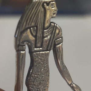 May include: Silver pendant featuring a detailed depiction of an Egyptian goddess with a headdress and an ankh symbol.