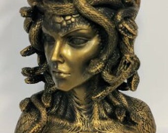 Puede incluir: Un busto de escultura de color dorado de Medusa, una figura mitológica griega con serpientes como cabello. La escultura está detallada con escamas de serpiente intrincadas y una expresión feroz.