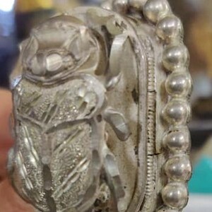 May include: A silver ring with a detailed beetle design. The beetle is made of clear crystal and is surrounded by a beaded band.