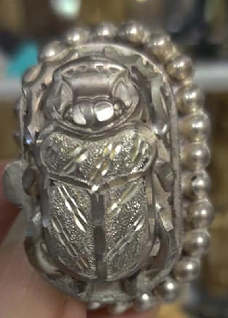 May include: A silver bracelet with a detailed beetle charm. The beetle is intricately carved and has a textured surface. The bracelet is made of small silver beads.