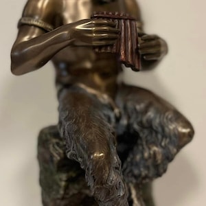 May include: A bronze sculpture of a satyr playing a pan flute. The satyr is seated on a rock and has a goat-like lower body with hooves. The sculpture is detailed and realistic.