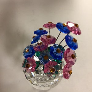 May include: A crystal vase with a clear glass base and a bouquet of pink and blue flowers. The flowers are made of crystal and have a faceted design.
