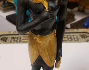 Peut inclure: Figurine noire et dorée d'un pharaon égyptien portant un couvre-chef et tenant un bâton. La base de la figurine est noire avec une inscription dorée qui dit "King Tut".
