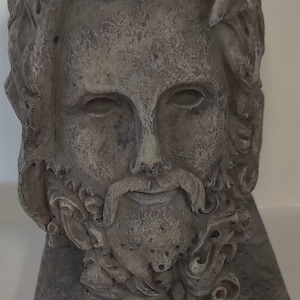 Puede incluir: Un busto de piedra gris de un hombre con barba y pelo largo. El busto está sobre una base cuadrada.