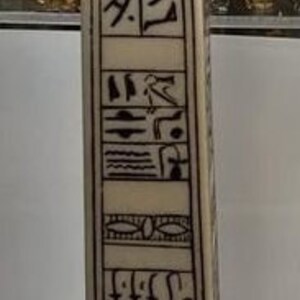 May include: A white obelisk with black hieroglyphics carved into the surface. The obelisk is on a white base and has the text "Made in Egypt" on the front.