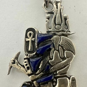 May include: Silver pendant featuring an Egyptian deity with blue enamel accents. The pendant has an ankh symbol and intricate details.