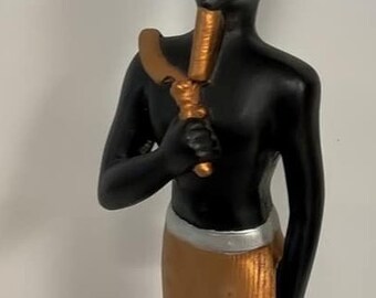 Peut inclure: Une figurine noire d'un pharaon égyptien portant une couronne dorée et rouge. Le pharaon tient un bâton doré et se tient sur une base en bois. La base porte une étiquette indiquant "Fabriqué en Égypte".