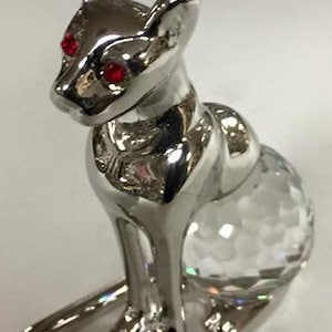 May include: A silver cat figurine with red rhinestone eyes and a clear crystal base.