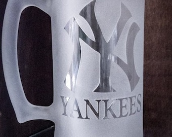 May include: Frosted glass beer mug with a handle. The mug features the New York Yankees logo and the word "YANKEES" etched into the glass. The mug is designed for cold beverages and is a fan item.