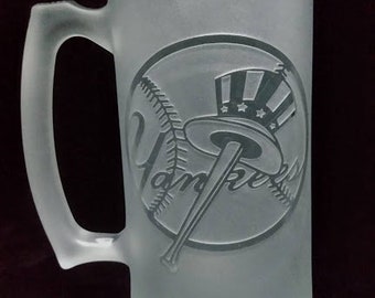 May include: Frosted glass beer mug with a handle. The mug features the New York Yankees logo, including a baseball, bat, and top hat. The design is etched into the glass. The mug is cylindrical and has a large handle.