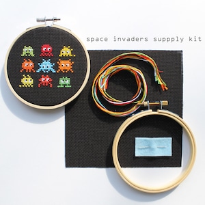 May include: A space invaders cross stitch kit with black Aida fabric, embroidery floss, a needle, and a wooden embroidery hoop.