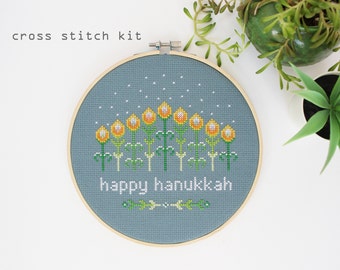 Puede incluir: Kit de punto de cruz con un fondo azul, una fila de flores amarillas y el texto "happy hanukkah" en blanco.