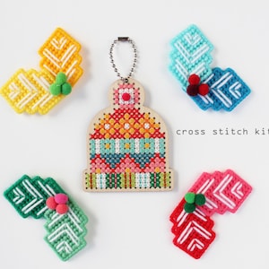 May include: A cross stitch kit with a central wooden ornament shaped like a hat, surrounded by four colorful, stitched leaf-like shapes. The hat and leaf shapes are in various colors, including yellow, blue, green, and red. The text "cross stitch kit" is also visible.