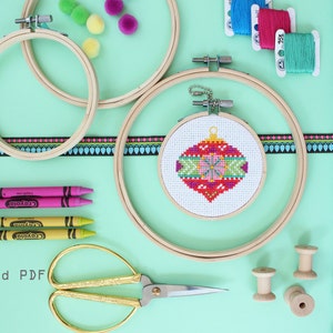 Peut inclure: Un kit de bricolage pour réaliser une décoration de Noël. Le kit comprend un petit cercle à broder avec un motif d'ornement rouge et vert pré-brodé, du fil à broder, une bobine en bois, des ciseaux, des crayons et des pompons bleus. Le texte "téléchargement instantané PDF" est également visible.