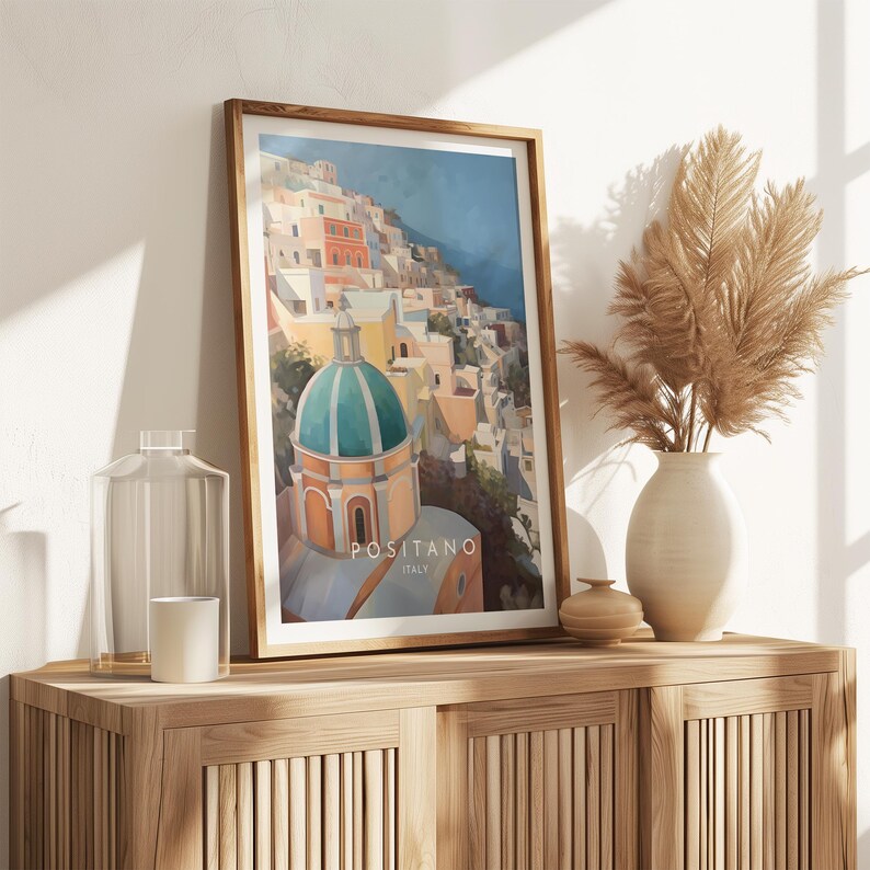 May include: A framed print of a colorful painting depicting a cityscape with a green-domed church in the foreground. The text "Positano, Italy" is printed below the image.