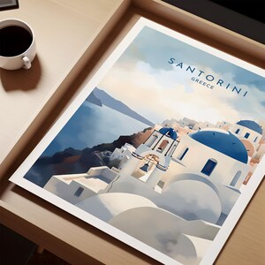 Puede incluir: Una impresi&oacute;n de Santorini, Grecia, con edificios blancos con c&uacute;pulas y detalles azules, sobre un mar y cielo azules. La impresi&oacute;n est&aacute; en una bandeja de madera, con una taza de caf&eacute; en la esquina.