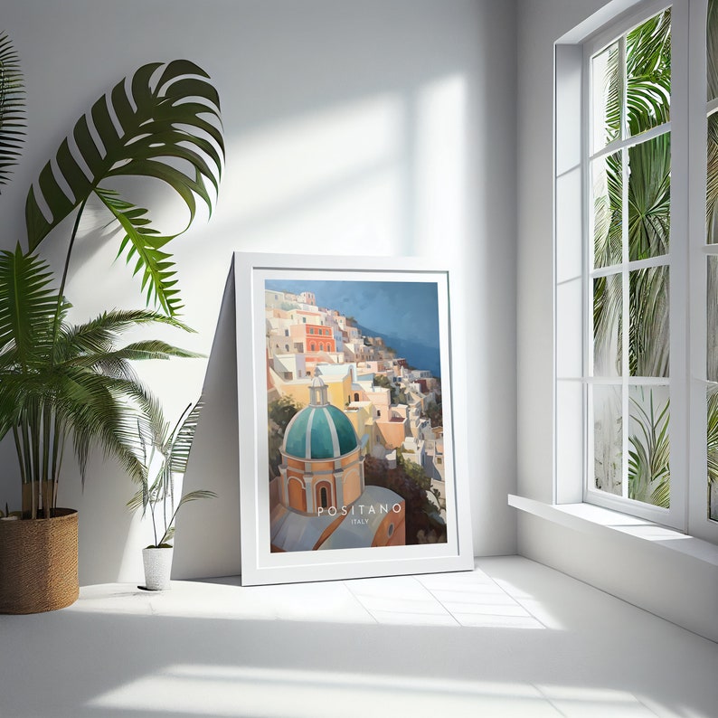 May include: A white framed poster with a colorful illustration of Positano, Italy. The illustration features a green-domed church building and colorful buildings on a hillside.