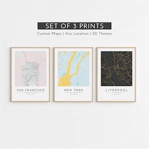 May include: A set of three framed wall art prints featuring map illustrations of San Francisco, New York, and Liverpool. Each print displays a city street grid with text labels for the city name, country, and coordinates on a white background.
