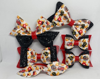 May include: A collection of handmade hair bows in various sizes. The bows feature a firefighter theme with a pattern of fire trucks, axes, and flames. Some bows are black glitter, others have red centers.