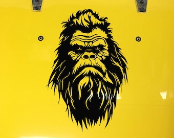 May include: Black and white silhouette of a Bigfoot or Sasquatch with a thick beard and long hair. The image is on a yellow background.