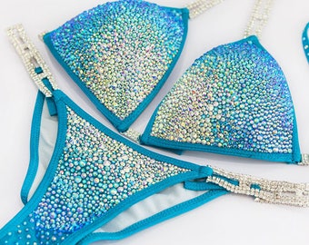 Könnte beinhalten: Ein türkisfarbenes Bikini-Set mit funkelnden, irisierenden Strasssteinen. Das Bikini-Oberteil und -Unterteil sind mit einem Farbverlauf aus Strasssteinen verziert, der von hellblau zu dunkelblau übergeht. Die Träger sind mit silbernen Strasssteinen besetzt.