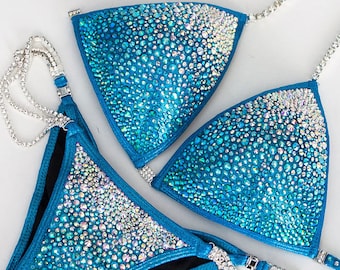 Könnte beinhalten: Ein türkisfarbener Bikini mit Kristallbesatz. Das Bikinioberteil und das Bikiniunterteil sind mit kleinen, schimmernden Kristallen besetzt, die einen glitzernden Effekt erzeugen. Der Bikini hat ein halterartiges Oberteil und ein hochgeschnittenes Unterteil.
