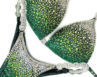 May include: A green and silver sequined bikini competition suit. The suit has a halter top and a high-cut bottom. The suit is covered in rhinestones.