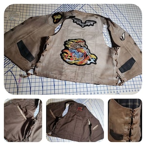 May include: A tan leather motorcycle vest with multiple patches, including a skull riding a motorcycle and a bat. The vest has a lace-up side and black accents. The vest is a biker-themed apparel item.