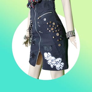 May include: Black denim skirt with a front zip, patches, and metal studs. The skirt features a skull graphic and a chain accessory. A punk rock style skirt.