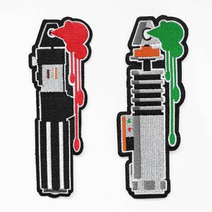 May include: Two embroidered patches depicting lightsabers, one with red dripping paint and the other with green dripping paint.