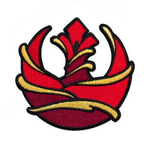 Może przedstawiać: Naszywka haftowana z symbolem Rebelii z Gwiezdnych Wojen. Symbol przedstawia stylizowanego ptaka z rozpostartymi skrzydłami, w kolorze czerwonym i złotym.