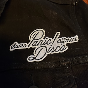 May include: Black denim jacket with a white embroidered patch that says "Same Panic! Different Disco".