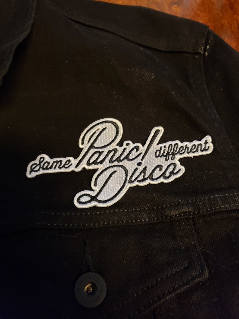 May include: Black denim jacket with a white embroidered patch that says "Same Panic! Different Disco".