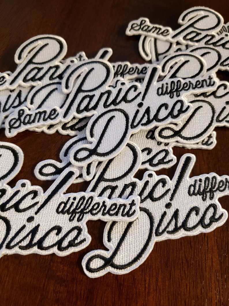 May include: A close-up of several white embroidered patches with black lettering. The patches read "Panic! Disco" and "Same Different".