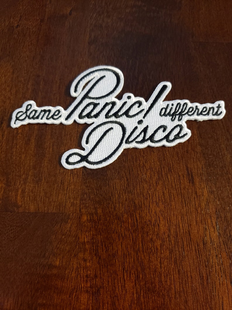 May include: White embroidered patch with black lettering that reads "Panic! Disco" with the words "same" and "different" on either side of the text.