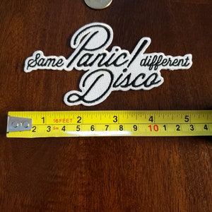 May include: White embroidered patch with black lettering that reads "Same Panic! Different Disco".