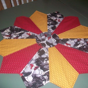 May include: A red and yellow table runner with a rooster print in the center. The runner is made of fabric and has a starburst design.