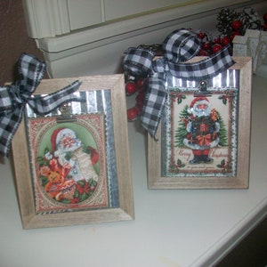 May include: Two rustic wood picture frames with metal accents, each featuring a vintage Christmas image of Santa Claus. One frame has a black and white checkered ribbon tied around it.