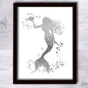 May include: A silver glitter mermaid silhouette with a shell in her hand, surrounded by silver glitter splatters on a white background.