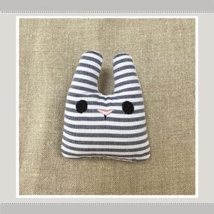 May include: A small, striped, grey and white stuffed bunny with black embroidered eyes and a pink nose.