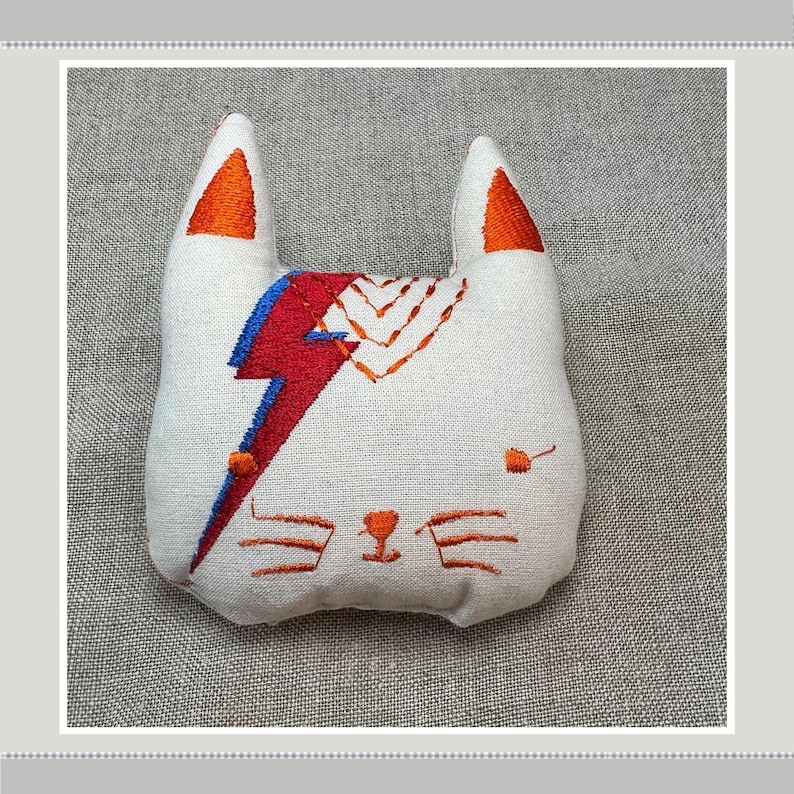 Catnip Cat Toy, David Meowie. David Bowie inspired cat toy. Cat face with red and blue thunderbolt and ginger facial detail on cream cotton fabric. Filled with premium Canadian Catnip and fibrefill. Soft, Durable and interactive for happy kitties. Enrichment gifts for cats and kittens.