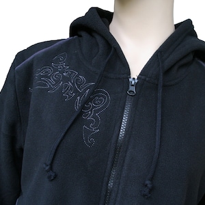 Könnte beinhalten: Schwarzer Kapuzenpullover mit Reißverschluss und einem dekorativen Stickmuster auf der Vorderseite. Der Pullover hat einen dunkelgrauen Besatz an den Schultern und einen kleinen Patch auf der rechten Schulter.