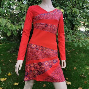 Könnte beinhalten: Ein rotes Langarmkleid mit einem geometrischen Muster aus Kreisen in Rosa-, Orange- und Blautönen.