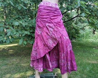 May include: A vibrant, layered skirt in shades of pink and magenta. The skirt features a unique, asymmetrical design with a ruffled hem and intricate geometric patterns. The fabric appears lightweight, suitable for warm weather.