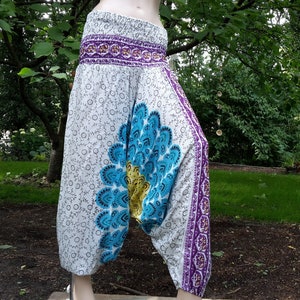 Könnte beinhalten: Weiße, blaue und lila bedruckte Hose mit Blumenmuster. Die Hose hat eine weite Beinweite und eine lockere Passform.