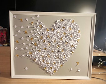 May include: A framed heart-shaped wall art piece made of white paper butterflies with gold accents.